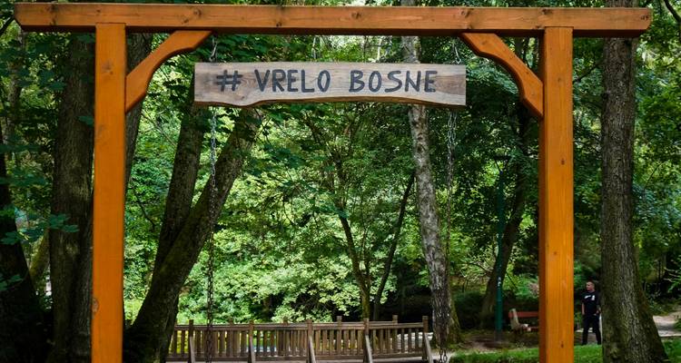 Un panneau en bois à l'entrée d'un parc avec des gens qui passent.