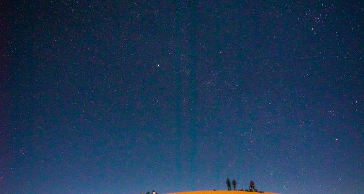 Ciel nocturne étoilé avec des silhouettes de personnes sur les dunes.