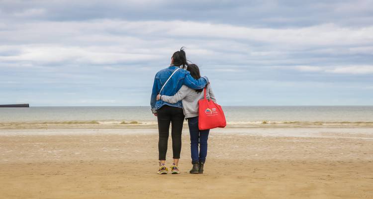 Two people standing on a beach facing the sea.