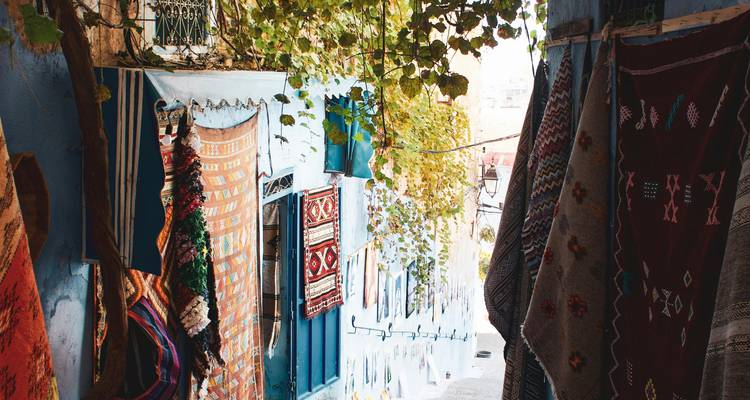 Des tapis colorés suspendus à l'extérieur dans une ruelle étroite à Chefchaouen.