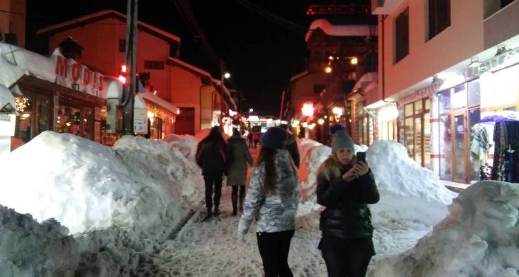 Scène de rue nocturne enneigée avec des personnes qui marchent.
