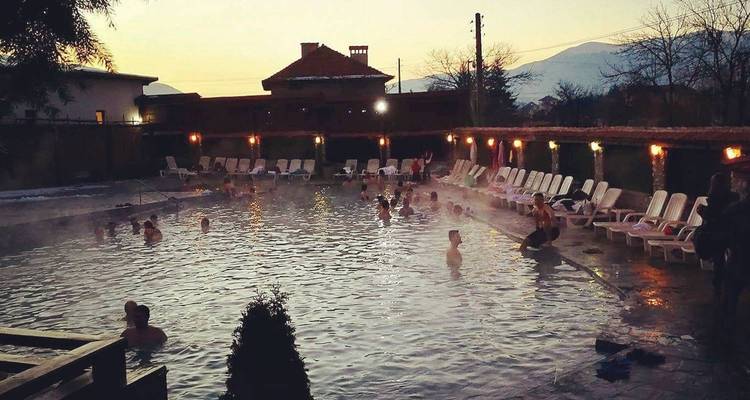 Des gens dans un bassin de source chaude au crépuscule avec des montagnes en arrière-plan.