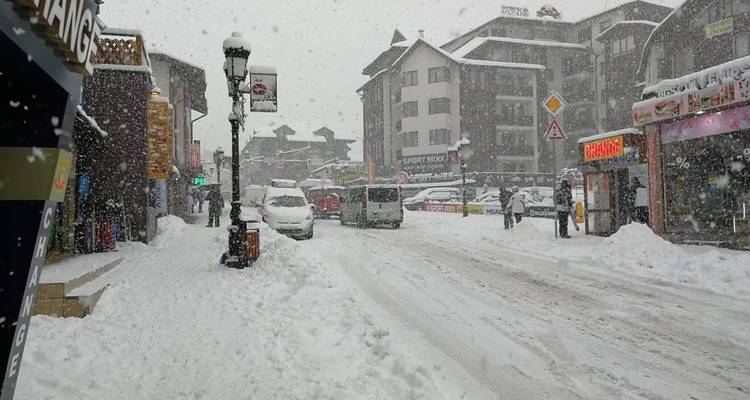 Une rue enneigée dans une ville avec des devantures de magasins et des voitures.