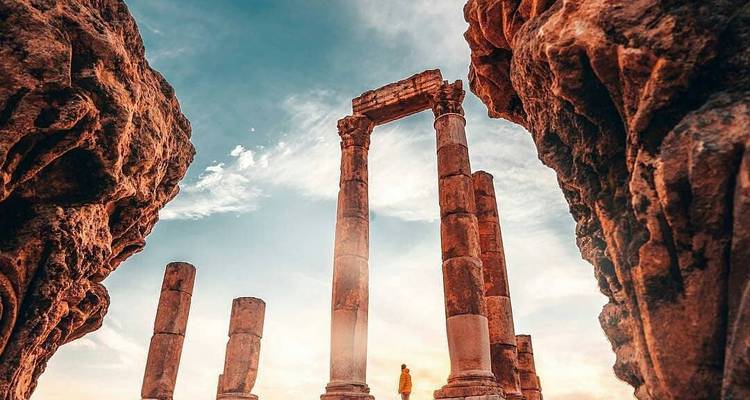 Eine Person, die durch antike Ruinen geht, die von Felsformationen eingerahmt sind.