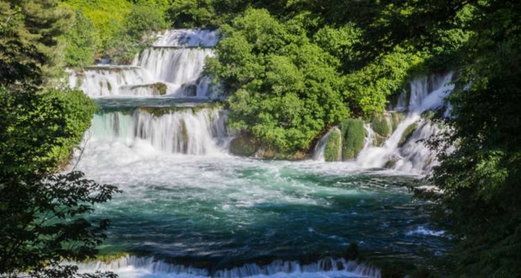 Cascade d'eau tombant sur des formations rocheuses entourées de verdure.