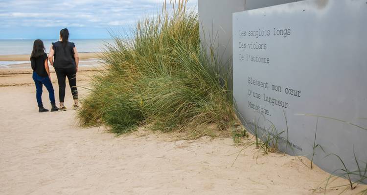 Deux personnes marchant sur une plage près d'un monument avec du texte gravé.