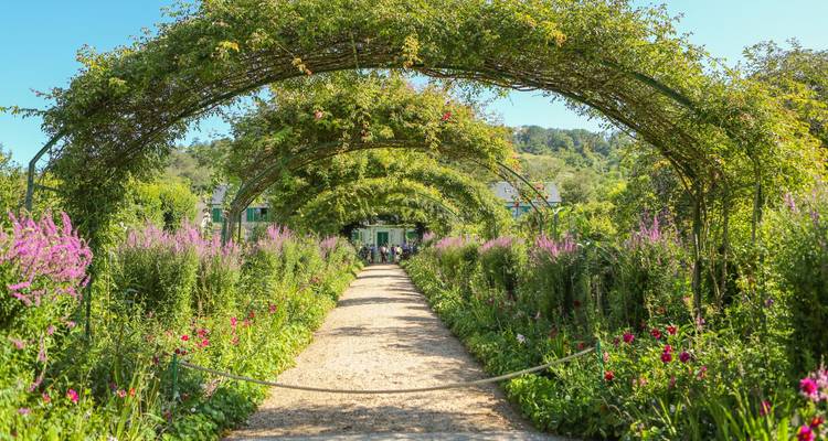 Schöner Gartenweg mit sich wölbendem Grün, der zu einem Gebäude führt.