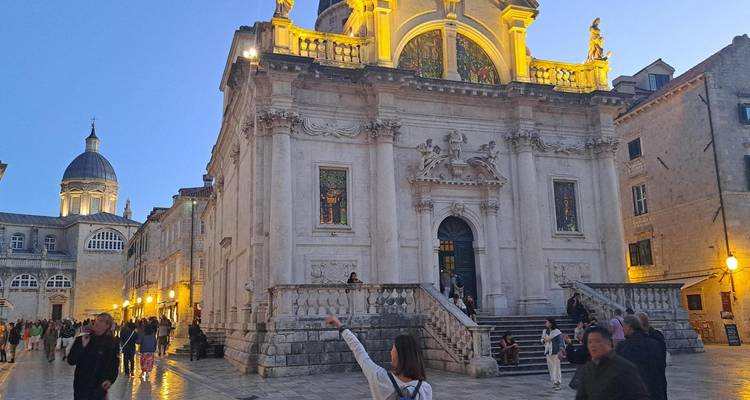 Escena nocturna en la Ciudad Vieja de Dubrovnik con la Iglesia de San Blas iluminada mientras los turistas exploran la plaza de mármol