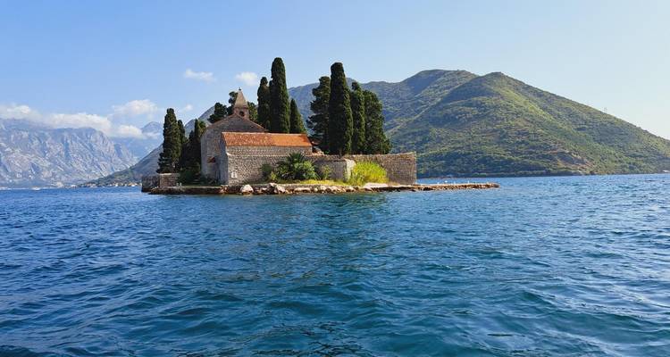 La isla del monasterio de piedra de Sveti Đorđe rodeada de cipreses se encuentra en las aguas azules de la Bahía de Kotor frente a montañas exuberantes