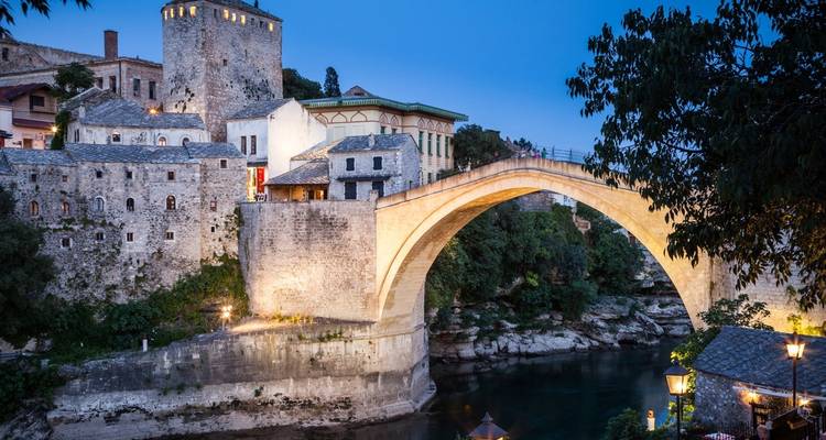 Puente de piedra sobre un río en una ciudad antigua al anochecer.