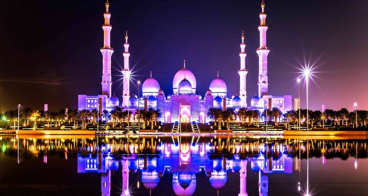 Illuminated mosque with reflection on water at night.