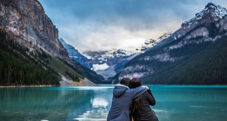 Twee mensen die elkaar omhelzen terwijl ze uitkijken over een turquoise meer en bergen.