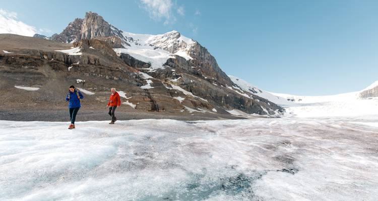 Twee mensen die op een gletsjer lopen met bergen op de achtergrond.