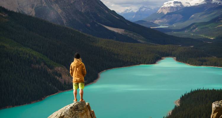 Persoon die op een rots staat en uitkijkt over een kronkelende, turquoise rivier in de bergen.