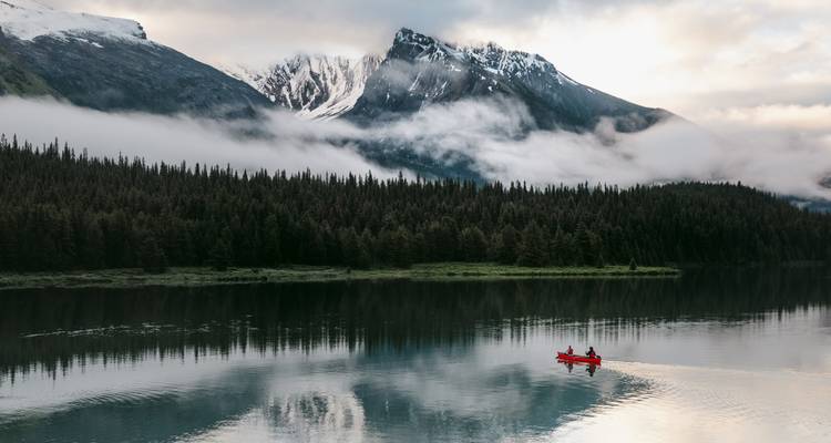 Twee mensen die kanoën op een rustig meer met mistige bergen op de achtergrond.