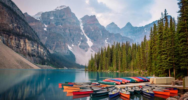 Kleurrijke kano's afgemeerd aan een serene meer met bergachtergrond.