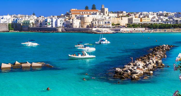 Leuchtend türkisfarbene Adria-Bucht mit Booten und Schwimmern vor der weißsteinigen Stadt Otranto.