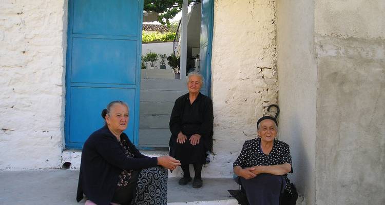 Tres ancianas sentadas a la puerta de una casa blanca.