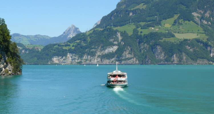 Boat cruising on a turquoise lake surrounded by mountains.