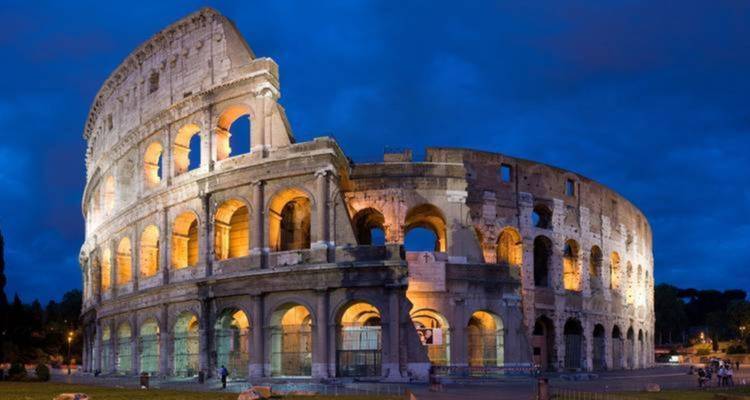 Colosseum in Rome lit up against a deep blue sky.
