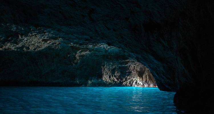 Grotte marine sombre avec eau bleue éclairée par la lumière naturelle.
