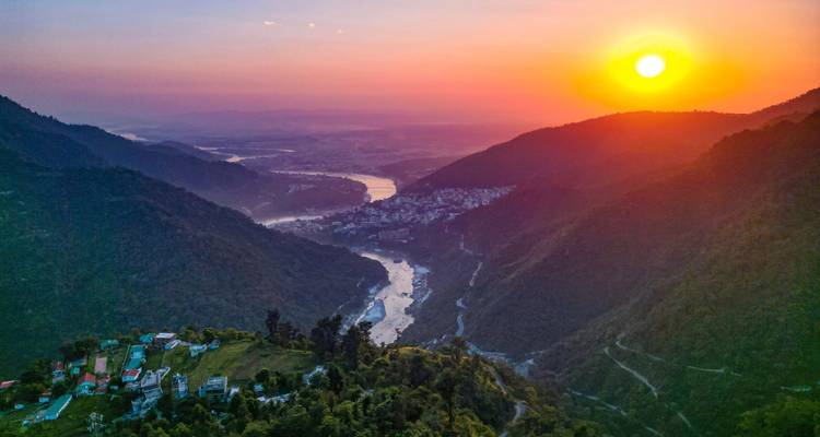 Vue aérienne d'une rivière traversant des montagnes au coucher du soleil.