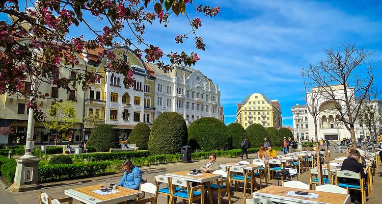 Terrasse de café en plein air avec des gens profitant du temps ensoleillé et des bâtiments historiques.