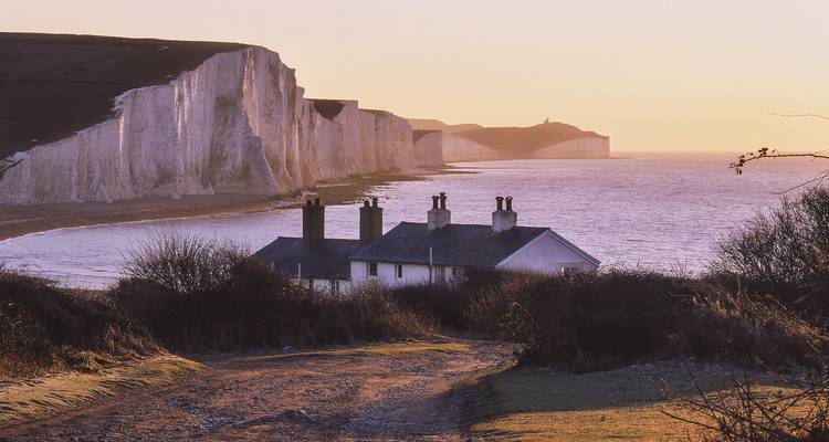 Falaises côtières et maisonnettes de plage au coucher du soleil.