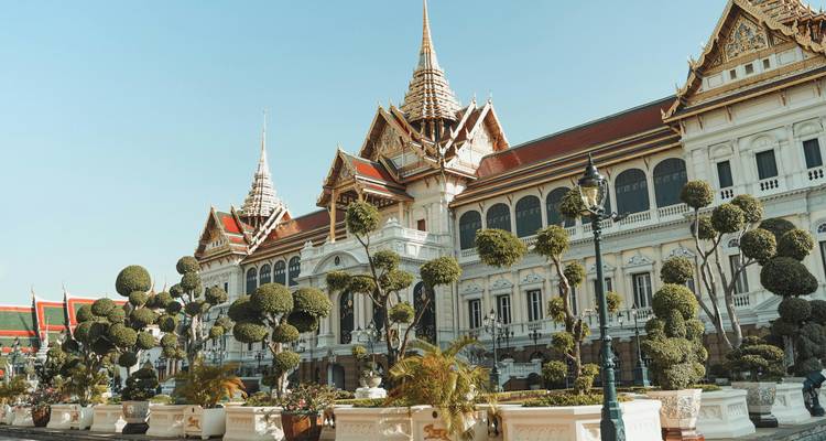 Complejo palaciego elegante de estilo tailandés con topiarios cuidadosamente recortados bajo un cielo despejado.