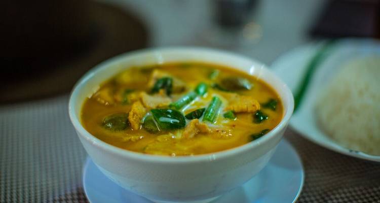 Bowl of curry with vegetables and rice on the side.