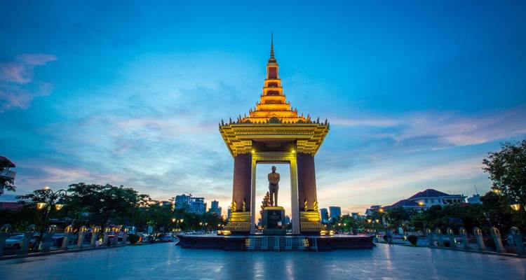 Monument in a city with a statue under a pagoda structure at sunset.