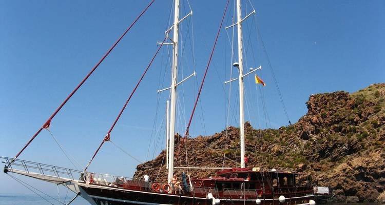 Gran velero atracado cerca de una costa rocosa.