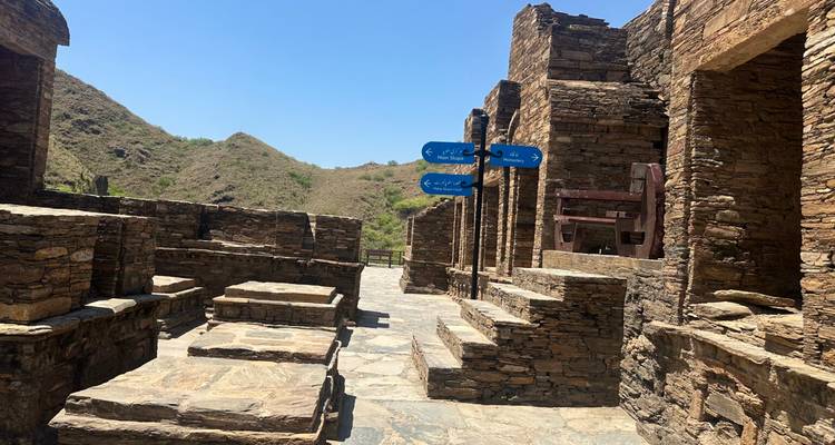Ruines anciennes avec des sentiers de pierre et une signalisation, situées dans un terrain montagneux.
