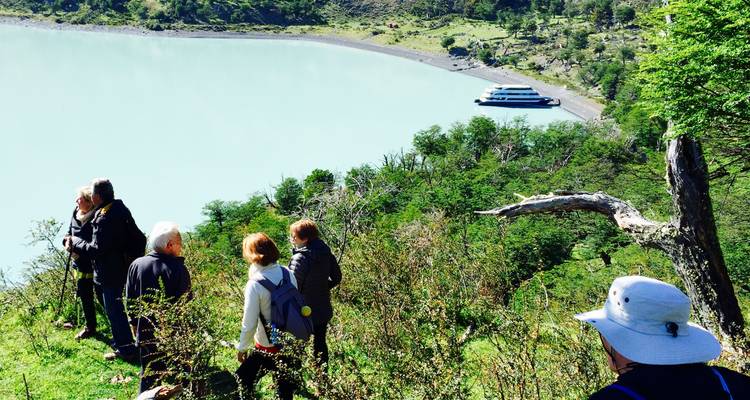 Randonnée en groupe au bord d'un lac turquoise et bateau de croisière.