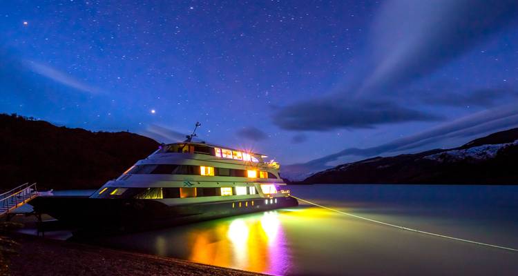 Navire de croisière illuminé sous un ciel étoilé au bord d'un lac.