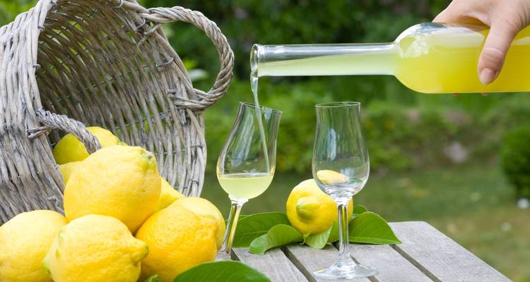 Gros plan de citrons et d'une bouteille versant une boisson au citron dans des verres sur une table en bois à l'extérieur.