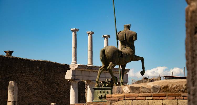 Statues et colonnes anciennes dans un site archéologique sous un ciel bleu dégagé.