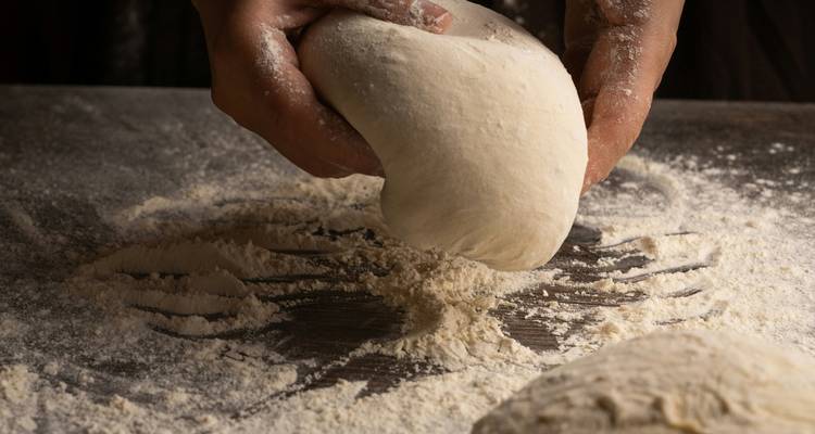 Gros plan de mains pétrissant la pâte sur une surface farinée.