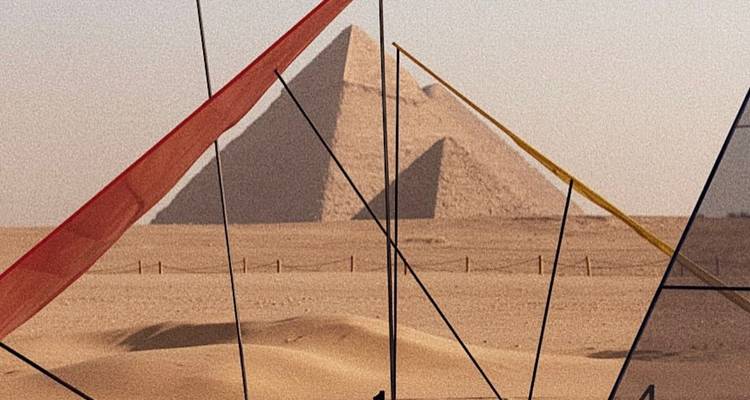 Scène de désert avec une pyramide visible à travers des bannières de drapeaux colorés.