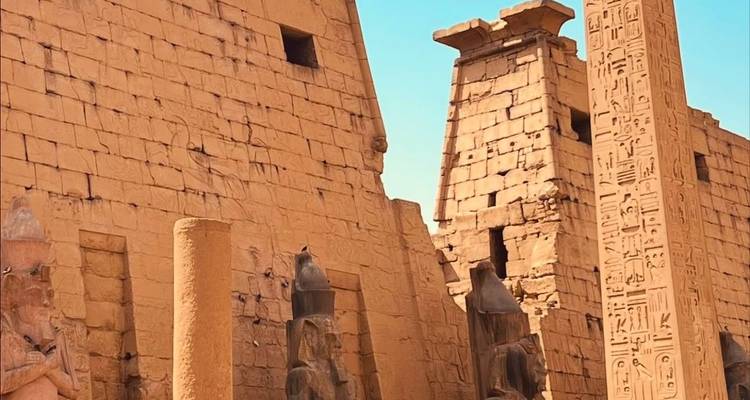 Temple égyptien antique avec statues et obélisque couvert de hiéroglyphes.