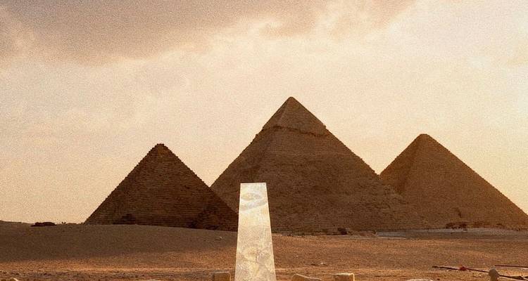 Vue panoramique des grandes pyramides de Gizeh avec une sculpture en verre au premier plan.