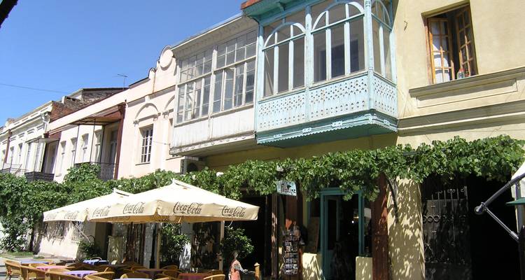 Charmante rue bordée de balcons couverts de vignes et de tables de café extérieures sous un ciel bleu dégagé