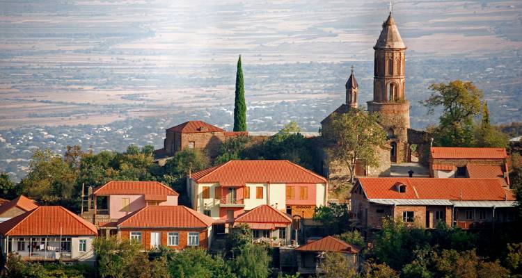 Village géorgien pittoresque perché sur une colline avec des toits en terre cuite et un clocher d'église élancé dominant une vaste plaine