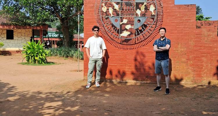 Two men posing in front of a wall with artistic design in an outdoor setting.