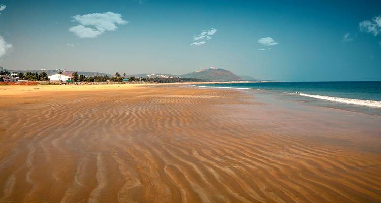 A wide sandy beach with distant hills under blue skies.