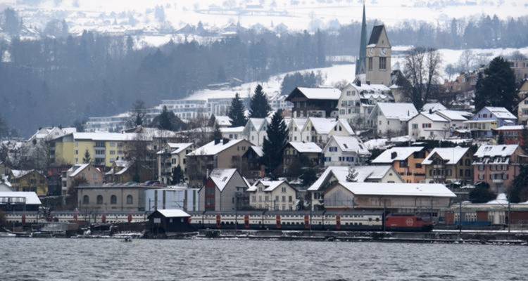 Snow-covered village with a church near a lake.