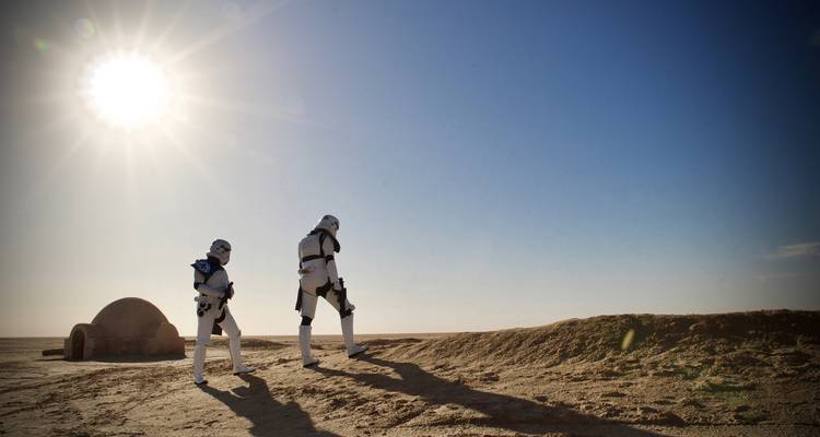 Des individus costumés marchant dans un paysage désertique sous le soleil.