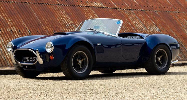 Klassischer blauer Sportwagen geparkt vor rostiger Struktur.