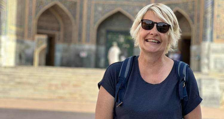 Glimlachende vrouw met zonnebril staat voor de ingang van een fraai betegelde madrasa.