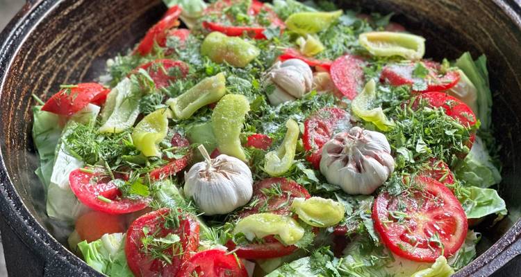 Close-up van een kleurrijke pot met verse groenten, tomaten, knoflook en kruiden klaar om te koken.